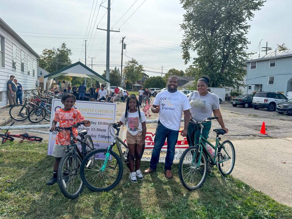 Pastor Elbert Harris giving a thumbs up beside a mother and two children with their new bikes at a CCT bike giveaway