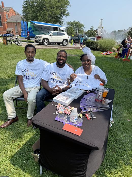 Pastor Harris and two CCT members at an outreach table with Let’s Win Together shirts and flyers