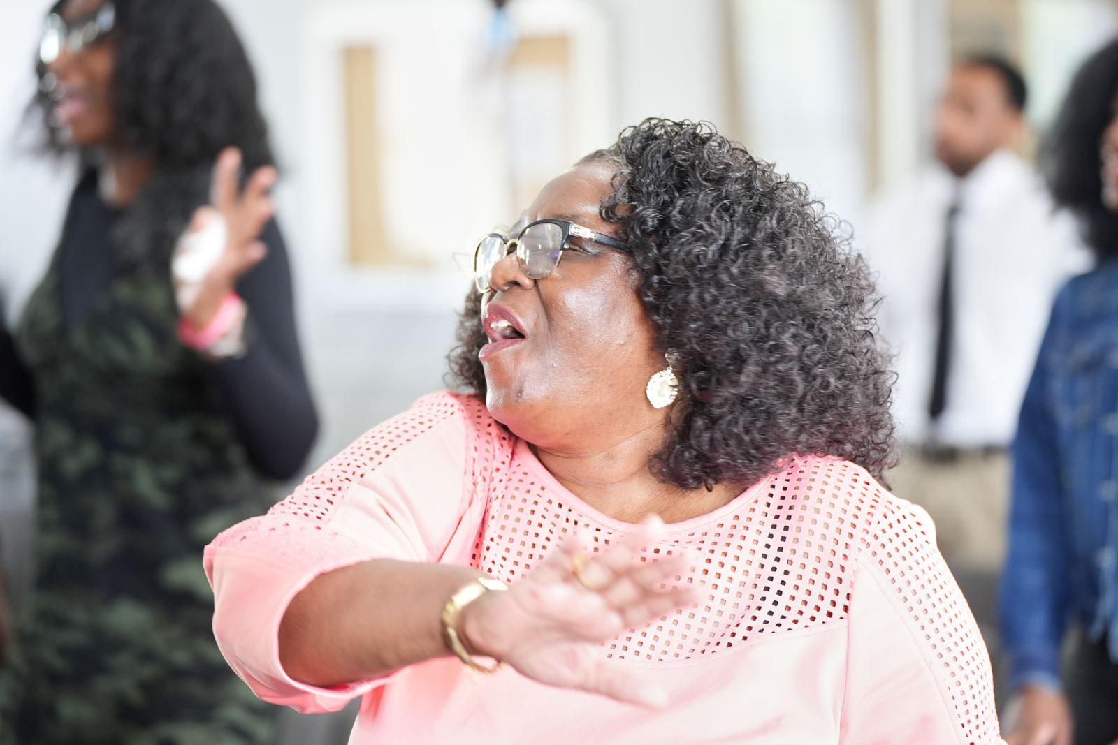 A woman in pink singing and worshiping joyfully during the service