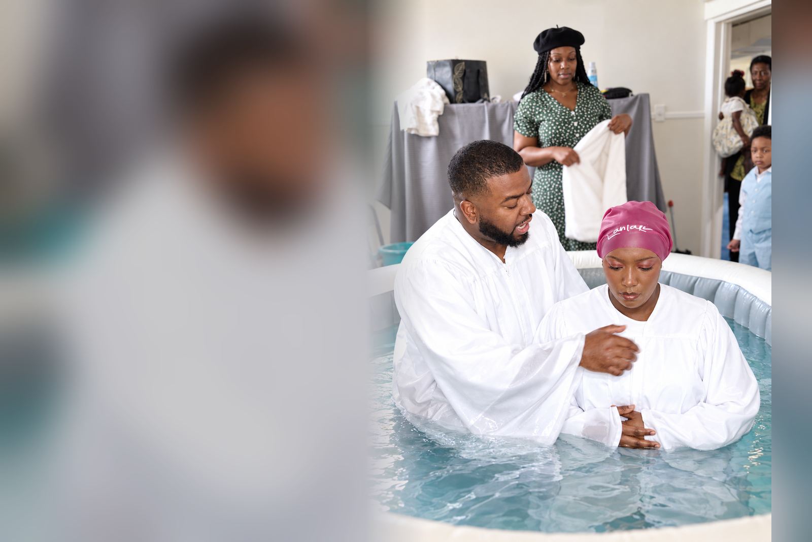Pastor Elbert Harris baptizing a woman in a white robe, as a church member waits nearby with a towel